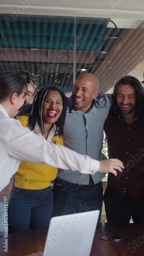 Vertical. Multicultural colleagues gather in a tight huddle around a table, smiling and cheering after good news in a bright modern office, expressing unity, motivation and collaborative spirit.