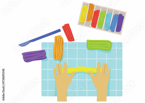 Hands stretching yellow clay on a blue grid surface, with other colored clay and a tool nearby.