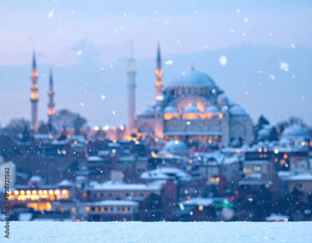Fototapeta premium Snow falling over Istanbul cityscape with mosque and minarets illuminated in the winter evening.