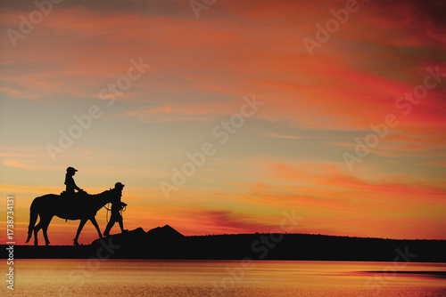 Young woman riding a horse, led by a horse trainer, at sunset. Arraial da Ajuda, Bahia, Brazil, 2022