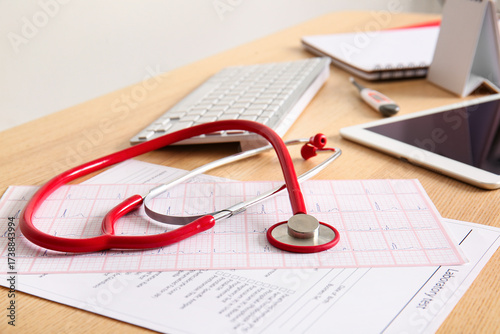 Stethoscope with cardiogram on wooden medical desk, closeup