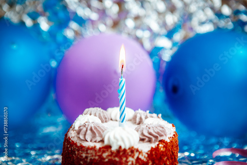 Happy birthday cake with burning one candle and blue and purple air balloons on silver background