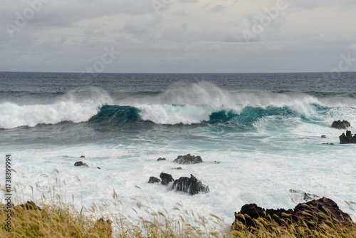 Waves crash on rugged rocks on serene Easter Island coast under clouds