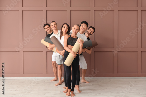 Group of sporty young people with yoga mats near brown wall