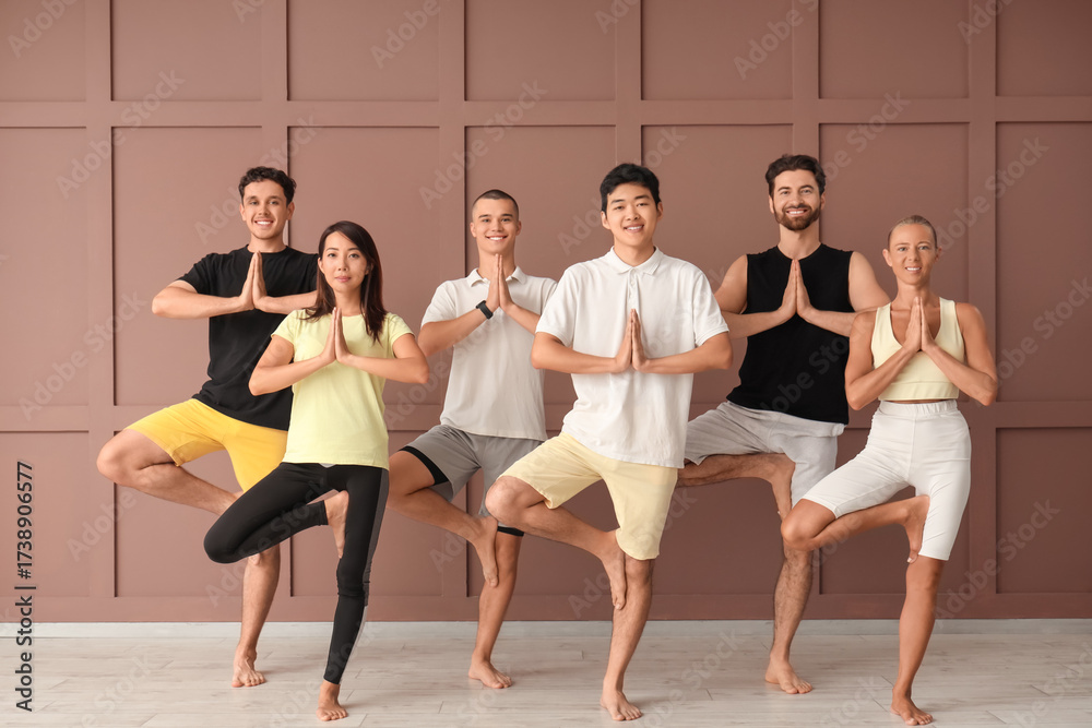 Naklejka premium Group of sporty young people practicing yoga near brown wall