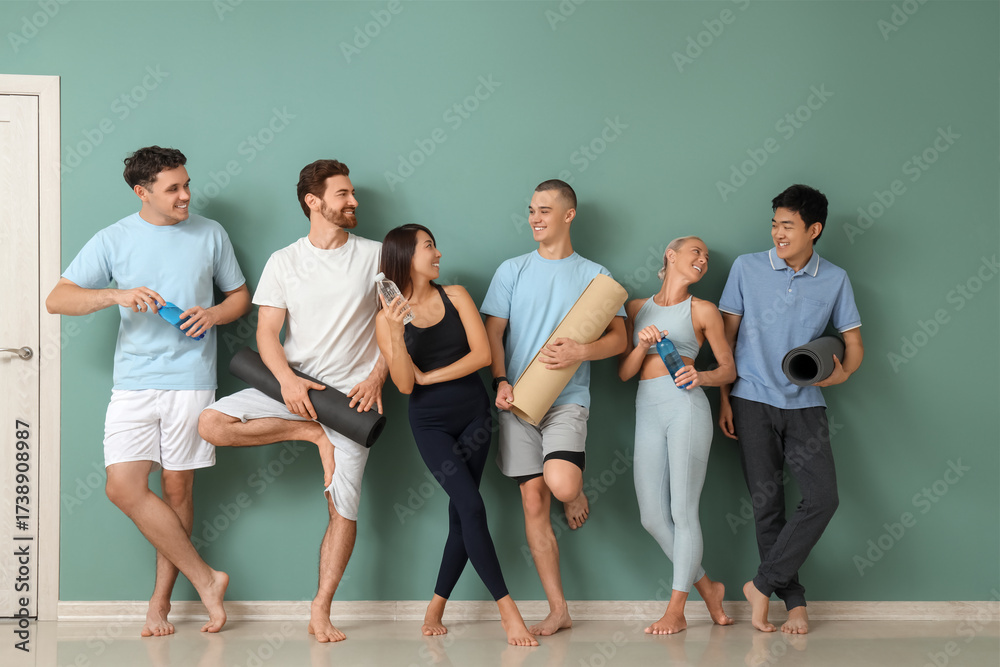 Fototapeta premium Group of sporty young people with yoga mats and water bottles near green wall