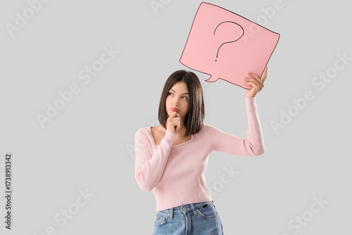 Thoughtful young woman holding speech bubble with question mark on light background
