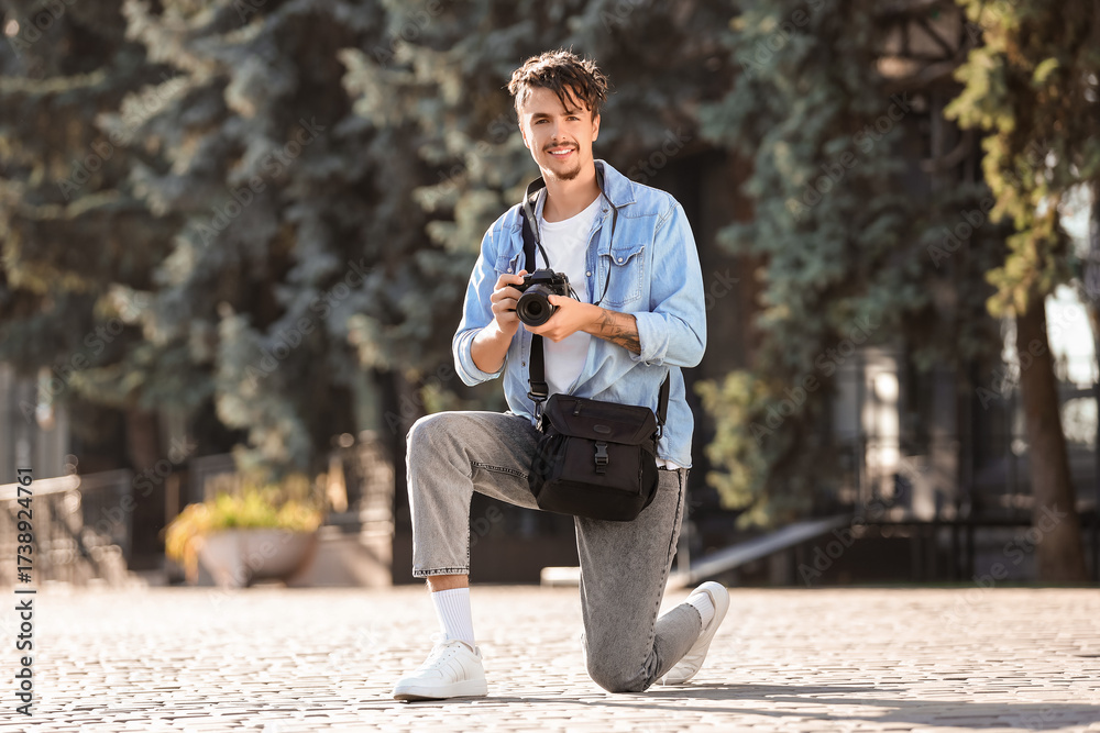 Obraz premium Young happy male photographer with camera and bag sitting in park