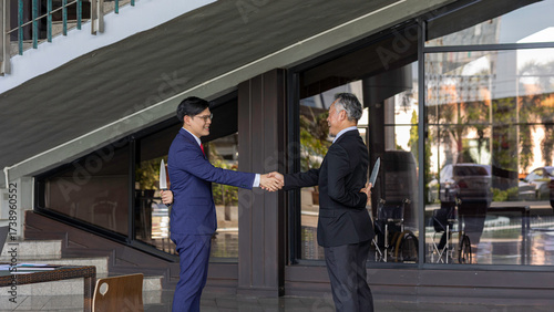 Fotografie Two businessmen shake hands while one hides a knife behind his back, symbolizing betrayal, deceit, backstabbing, and the dangers of trust and dishonesty in business relationships