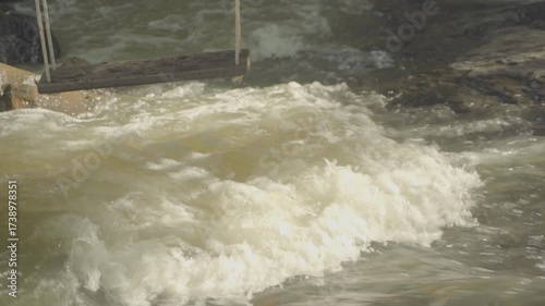 A ungraded zoomed medium to close shot a a river cascade seeing the turbulent water and the swing on the left top.