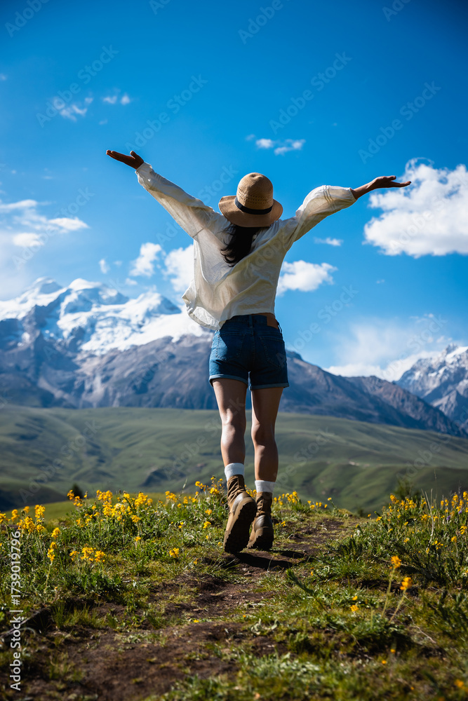 Fototapeta premium Woman open arms to snowcapped mountain on sunset grassland mountain top