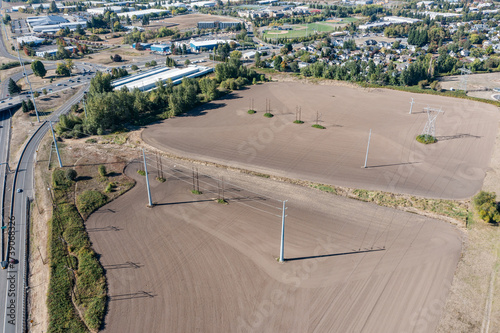 4K aerial drone photo of farmland with high voltage power transmission lines in Hillsboro Oregon, showing cultivated soil fields, tall pylons, and surrounding industrial and suburban landscape  