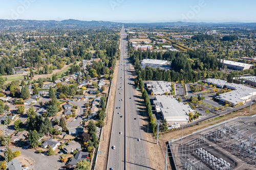 Aerial drone picture of traffic on US 26 highway in Hillsboro Oregon during a clear fall day, showing multiple lanes of cars and trucks moving under blue sky with surrounding suburban and rural are