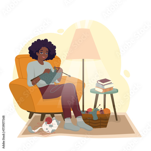 Woman sits in an armchair knitting with a gray cat nearby, creating a cozy home atmosphere. A basket of yarn and books complement the setting. Vector illustration captures relaxation.