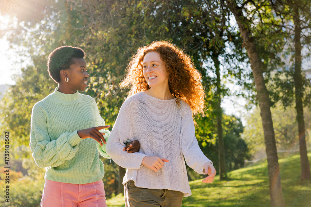 Fototapeta premium two young women smiling and talking during a walk at park, concept of friendship and friends enjoying time together, copyspace for text