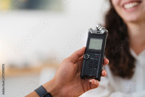 A person holds a digital audio recorder, capturing sound during an interview with a smiling woman.