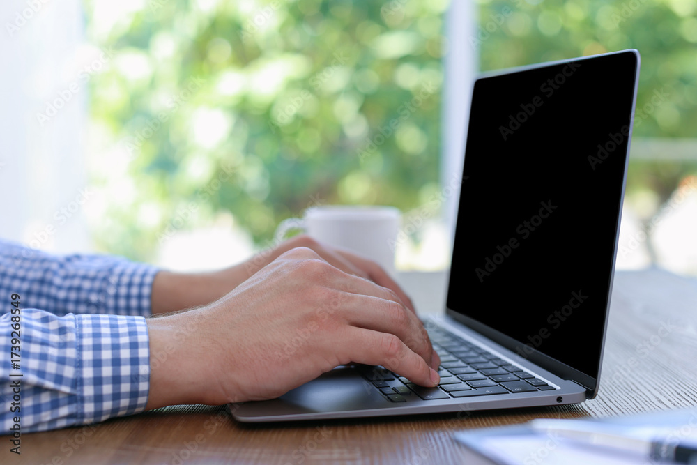 Fototapeta premium Man working on laptop at wooden table indoors, closeup