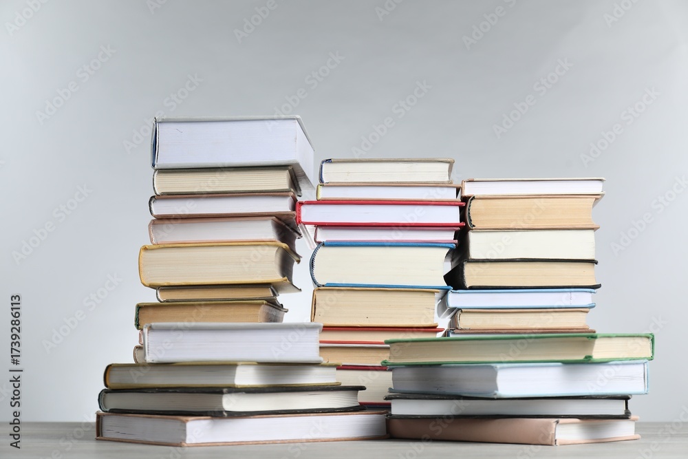 Fototapeta premium Many stacked books on table against light grey background