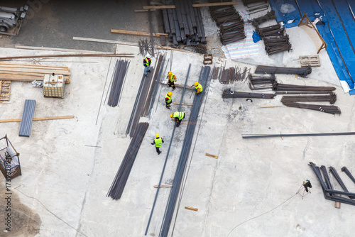 Construction Site Workers Arranging Steel Rebar and Materials on Large Open Work Area