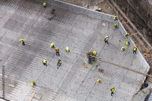 Construction Workers Cooperate On Reinforcement Grid Across Foundation At Busy Site