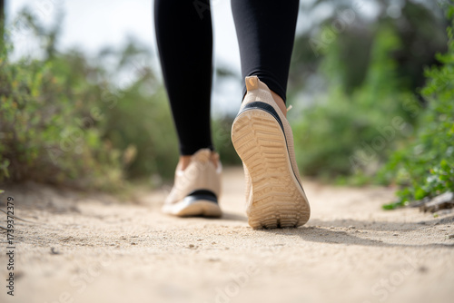 Close-up of a person's feet in sneakers walking on a dirt trail surrounded by greenery, capturing movement and outdoor exercise, fitness activity and nature trail exploration.