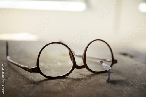 Glasses on a table with a miniature woman looking through the lens, beyond boundaries.