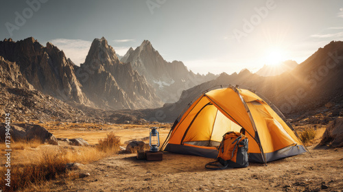 Camping adventure in mountains with tent and backpack under the sunset. Vibrant image capturing a camping scene with orange tent, backpack, and lantern set against majestic mountains during sunset