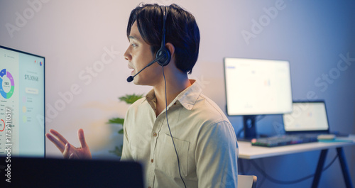 Asian businessman call center agent with headset working at night in a modern office, using computer to help customers — IT support, clear communication and professional service.