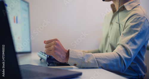 Close-up of hand typing on computer keyboard with monitor showing business data and charts at night in office workspace.