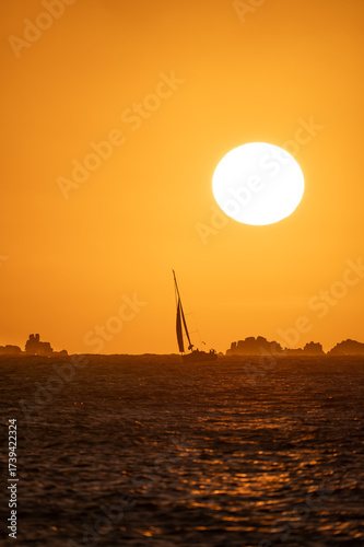 A sailboat in a golden-hour sunset with a few rocks in the background	