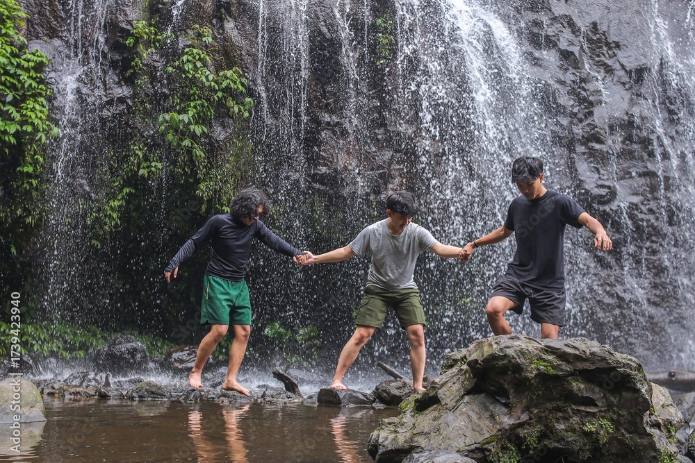 Obraz premium Three Friends Joyfully Exploring Vibrant Waterfall Nature Together During Summer Travel