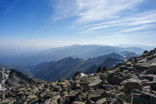 Expansive panoramic view over rocky peaks and mountain ranges of Sierra de Gredos, Spain, with distant layers under a blue sky and soft clouds, capturing wild and rugged highlands.