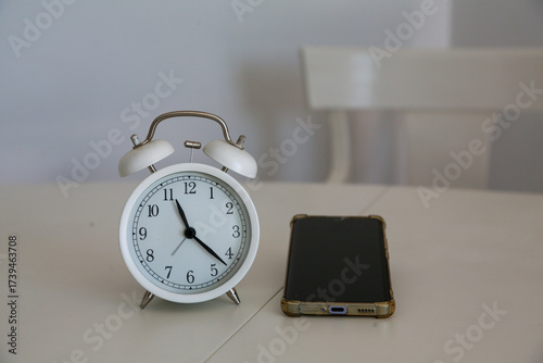 An analogic clock next to a mobile phone on a white background symbolizes the passage of time spent in front of screens. Concept: social issues