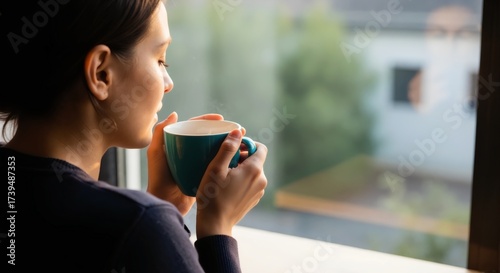 Woman enjoying a hot coffee by the window in the morning. Person savoring a quiet moment with a warm beverage. Daily ritual and simple pleasures concept with copy space