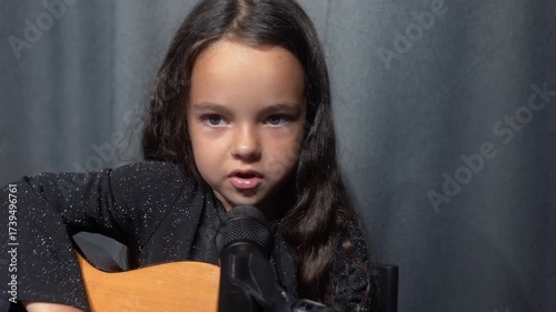 Portrait of a little singer plays the guitar and sings a song on stage. Beautiful voice. Live music concert show.