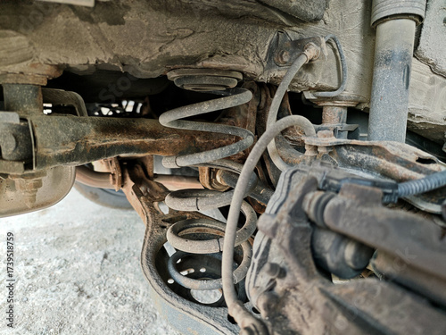 фотографія Close-up of a dirty and rusty car undercarriage showing the coil spring suspension, shock absorber, and brake caliper during a mechanical inspection
