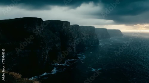 Jagged cliffs meet stormy ocean under an overcast sky. A dramatic, moody landscape scene