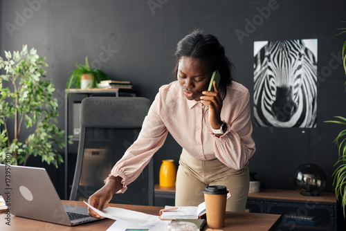 Young black businesswoman multitasking on phone call in modern office