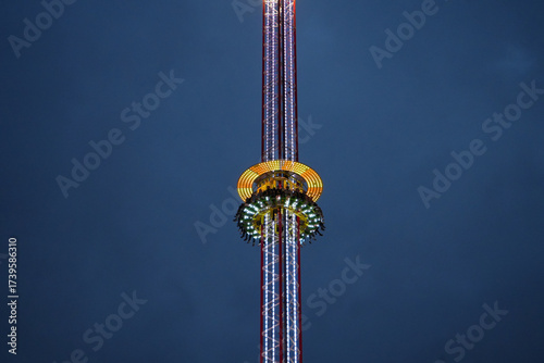 People enjoying an illuminated amusement park drop tower ride against a twilight sky at Goose Fair, Nottingham, England.