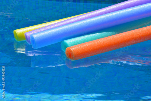 Colourful pool noodles floating on water in swimming pool