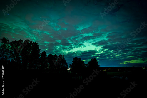 Northern lights dancing behinde the dark cloud over country landscape