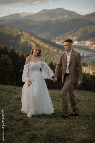 A beautiful, happy young couple in love on a wedding walk and photo shoot high in the mountains. The groom in a jacket and suit and the bride in a white dress at a resort. Kissing and hugging