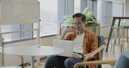 Senior Asian businessman wearing headset celebrates success during online meeting in modern co-working space. Remote work and business communication concept	