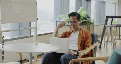 Senior Asian businessman wearing headset celebrates success during online meeting in modern co-working space. Remote work and business communication concept	