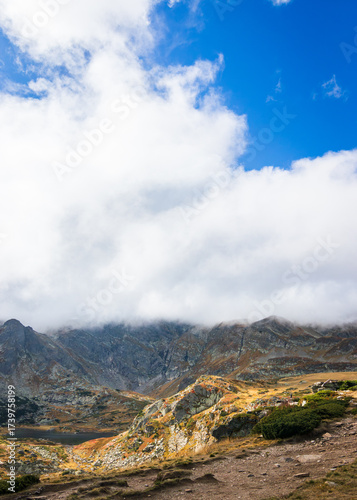 Mountain landscape with blue sky and clouds. A tinny lake is located at the bottom of the mountains.