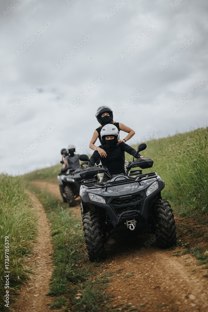 Fototapeta premium Friends wearing protective gear ride all-terrain vehicles through a scenic countryside path, experiencing adventure and group fun.