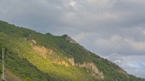 Sunny granite mountain top with trees against a dark cloudy sky in La Vanoise national park, Savoie, France 