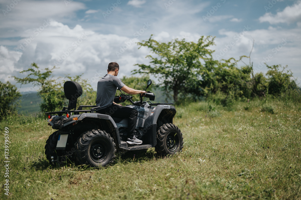 Fototapeta premium A single man enjoying a quad bike ride on a green landscape with trees and clouds, perfect for outdoor adventure themes and recreational images.