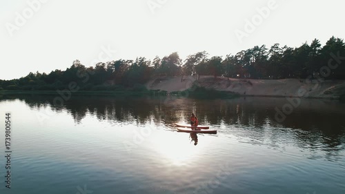 Aerial view of two young women paddling down river on SUP boards against backdrop of steep white bank and pine forest. Concept for trendy sport and active recreation