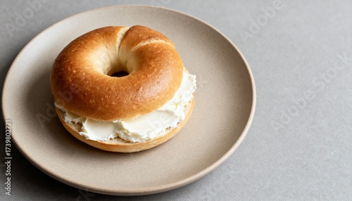 Golden bagel with a thick layer of cream cheese on a ceramic plate—simple, cozy breakfast in soft natural light.
